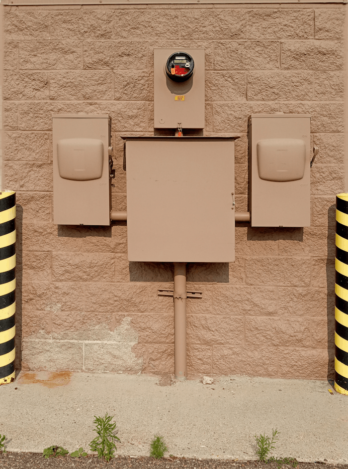 Industrial electrical fuse box with warning stripes on an urban wall.